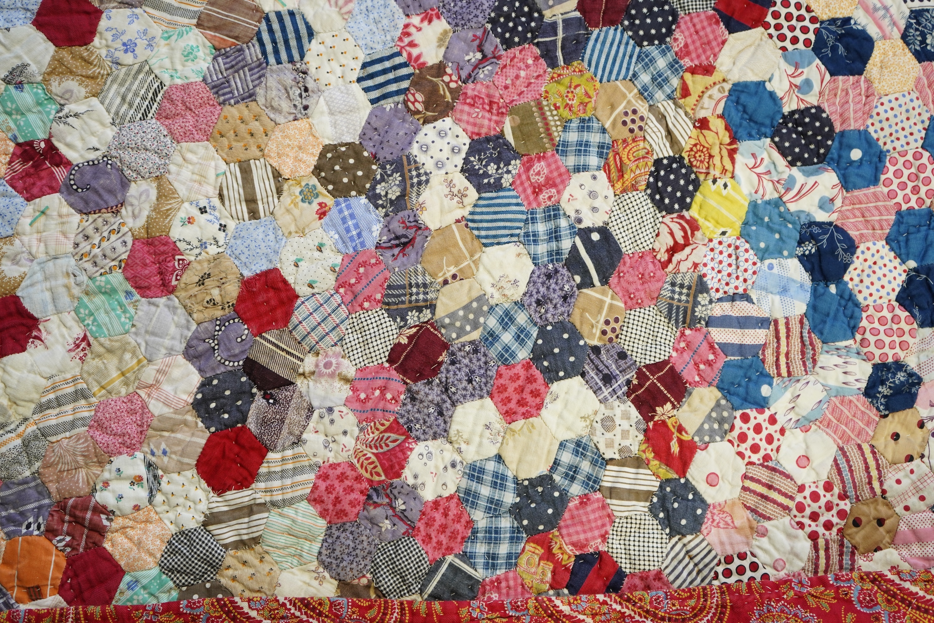 An English cotton hexagon hand made and hand pieced quilt, made from a large variety of printed dress fabrics from 19th century. The quilt edged with a wide stripped multi fabric border. The under side designed in wide s